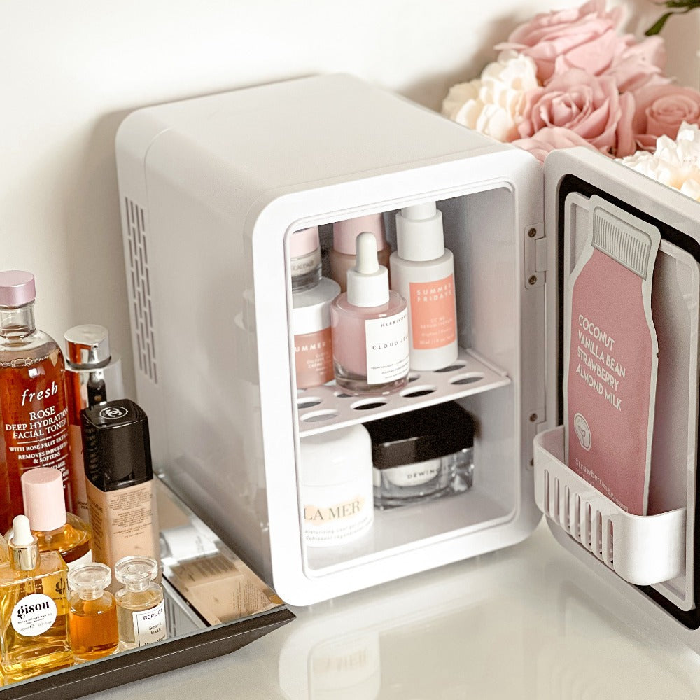 The White Marble Cosmetics Fridge on a vanity table filled with luxury skincare products and sheet mask. Nexy to flowers and makeup, cosmetics and perfume